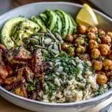 A steaming Vegetable and Legume Bowl features golden roasted broccoli and cherry tomatoes over quinoa with a creamy tahini drizzle.