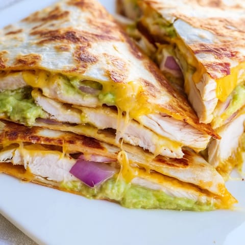 A sizzling skillet holds a freshly made Chicken Avocado Quesadilla, topped with fresh cilantro and red onion, ready to be served with lime wedges.