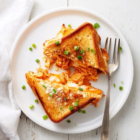 Freshly grilled Buffalo Chicken Ranch Grilled Cheese cut diagonally, revealing a gooey ranch and cheese center, served on a rustic wooden cutting board.