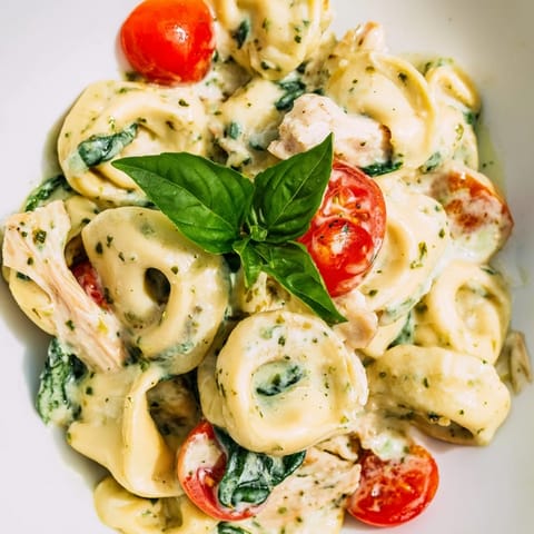 Golden cheese tortellini and tender chicken tossed in a creamy pesto sauce, served steaming in a skillet for dinner.