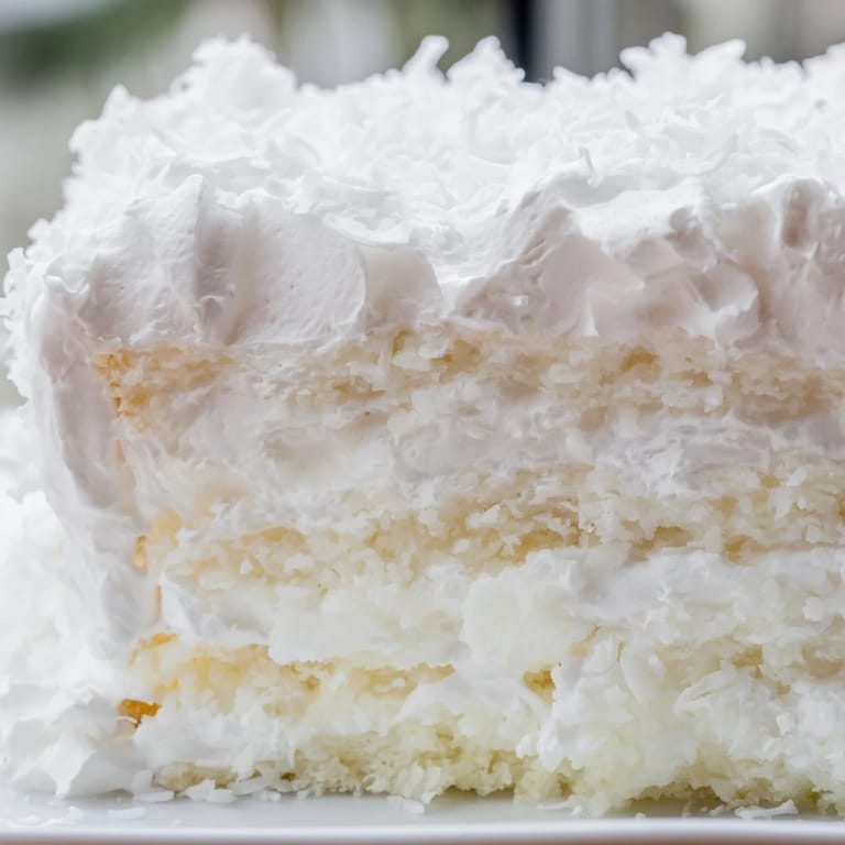 A slice of golden Coconut Cake with coconut filling and cloud-like frosting, ready to enjoy.