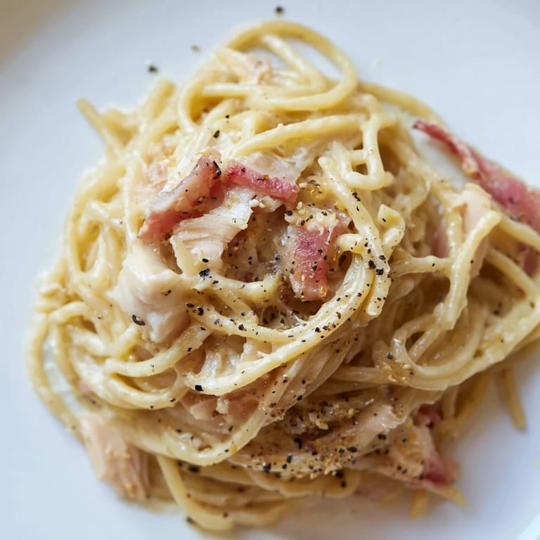 Homemade chicken carbonara served on a white plate, garnished with fresh parsley and extra grated Parmesan cheese.