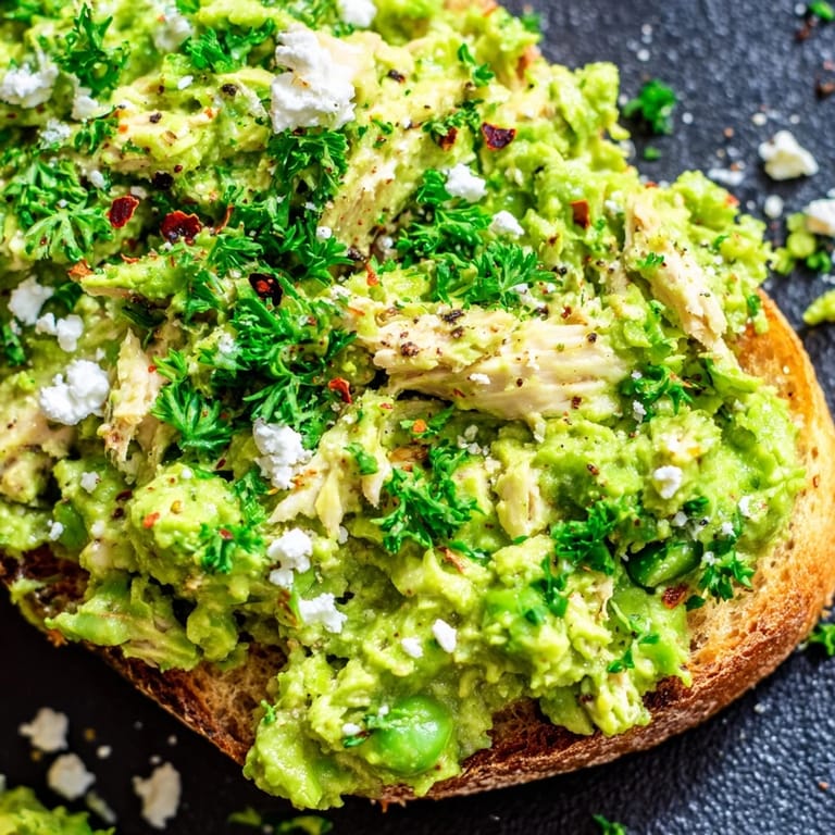 Served on a wooden board, Smashed Pea & Chicken Toast offers a satisfying blend of crispy bread, savory chicken, and bright mint, perfect for a quick lunch.