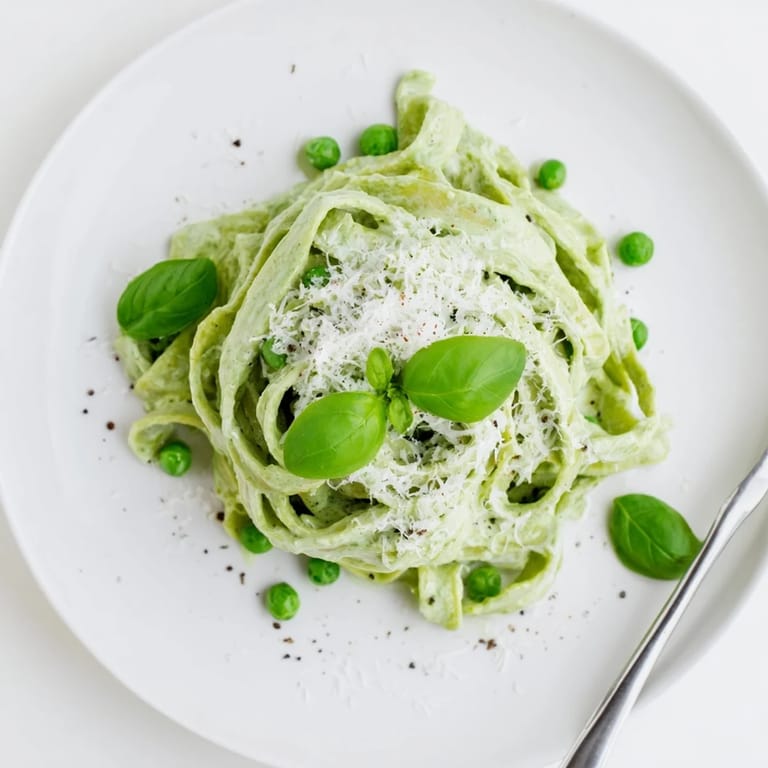 A skillet of bubbling green pea alfredo sauce blended into silky pasta, ready to serve for a comforting weeknight dinner.  