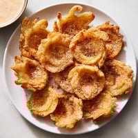 Golden, crispy onion petals blooming on a plate, served with a vibrant, spicy dipping sauce.