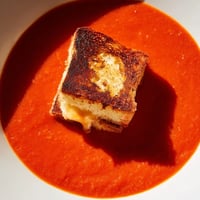 A bowl of creamy roasted tomato soup topped with golden, crispy grilled cheese croutons for a cozy meal.  