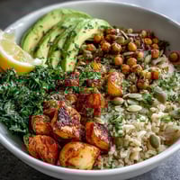 Roasted red bell peppers and zucchini top a hearty Vegetable and Legume Bowl garnished with avocado and parsley.