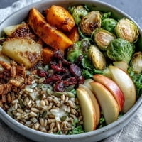 A colorful autumn harvest bowl with roasted butternut squash, Brussels sprouts, kale, and apples served over hearty farro.  