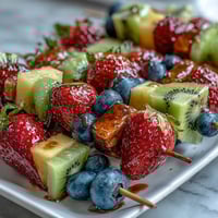 Vibrant rainbow fruit skewers featuring strawberries, pineapple, kiwi, and grapes, served with a creamy honey-yogurt dip for a refreshing summer treat.